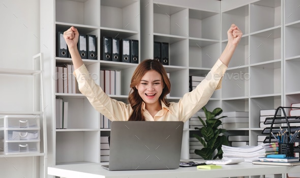 Beautiful young teen asian businesswoman holding computer laptop with hands up in winner is gesture, Happy to be successful celebrating achievement success